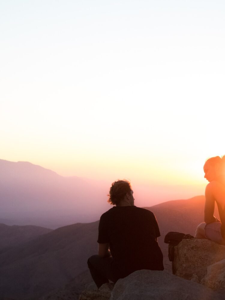 two sitting and one man standing near cliff taken during golden hour